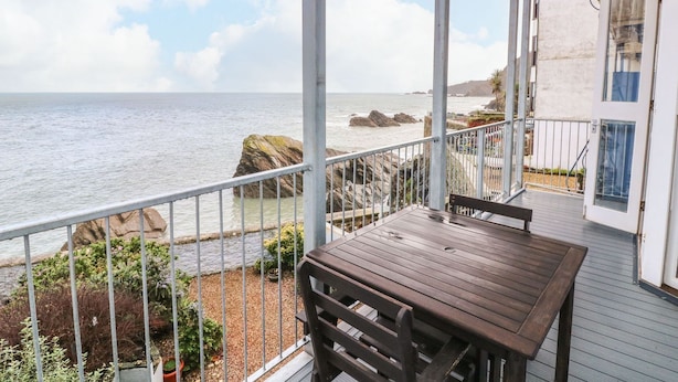 Ein Holztisch und eine Bank auf einem Balkon mit Blick aufs Meer.