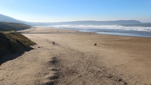 Ein weiter Sandstrand mit sanften Wellen, einem klaren Himmel und Hügeln in der Ferne.