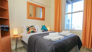 Ein Hotelzimmer mit Bett, Nachttisch, Spiegel und einem Fenster mit Vorhängen.