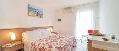 A hotel room with a bed, bedside tables, a desk, a chair, and a window with curtains.
