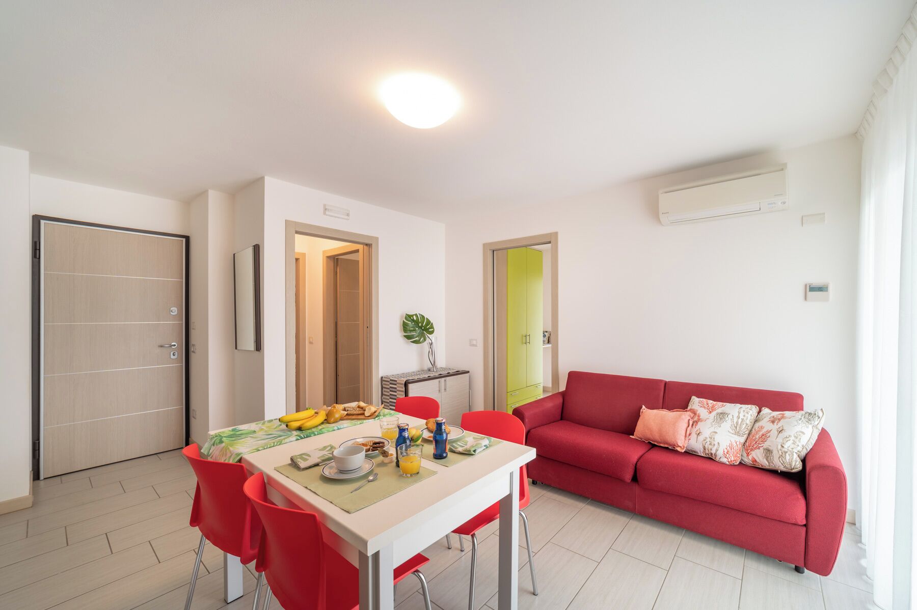A modern living room with a red sofa, a dining table with breakfast items, and a bright ceiling light.