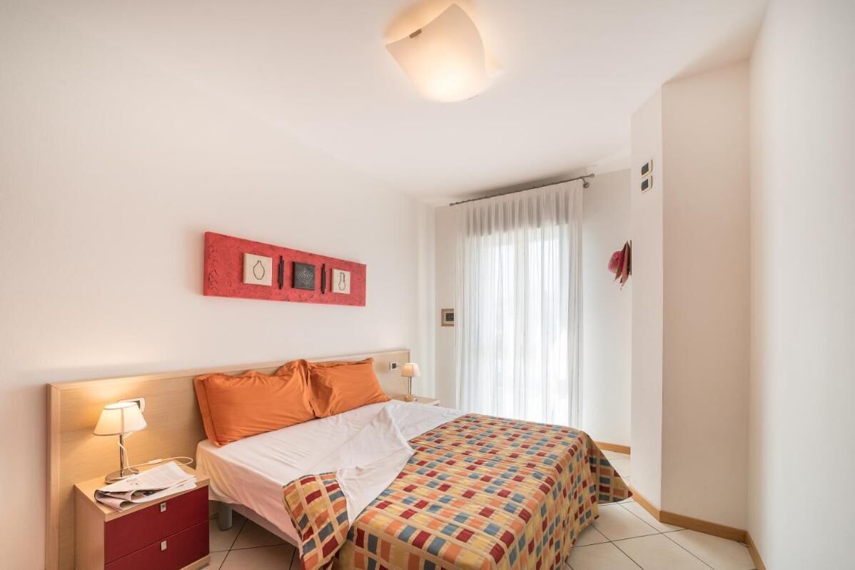A hotel room with a bed, a nightstand, a lamp, a window with curtains, and a wall with three framed pictures.