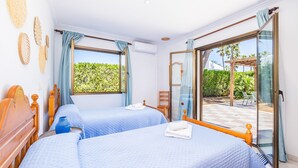 A hotel room with two beds, a large sliding glass door to a patio, and a view of greenery outside. - Holiday Home 'Llenaire Gran Beach House' with Mountain View, Wi-Fi and Air Conditioning (Pollença)