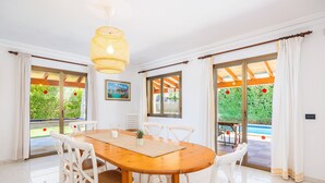A dining area with a wooden table, white chairs, and a hanging light fixture. - Holiday Home 'Llenaire Gran Beach House' with Mountain View, Wi-Fi and Air Conditioning (Pollen ça)