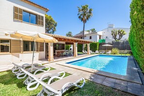 A swimming pool with lounge chairs, a covered patio, and a well-maintained lawn.