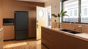 Una cocina moderna con armarios de madera, un refrigerador negro, un microondas integrado, un lavamanos con detalles dorados y una planta en maceta sobre la encimera.