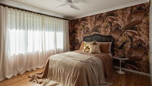 Un dormitorio con cama, cortinas, ventilador de techo y papel tapiz tropical.