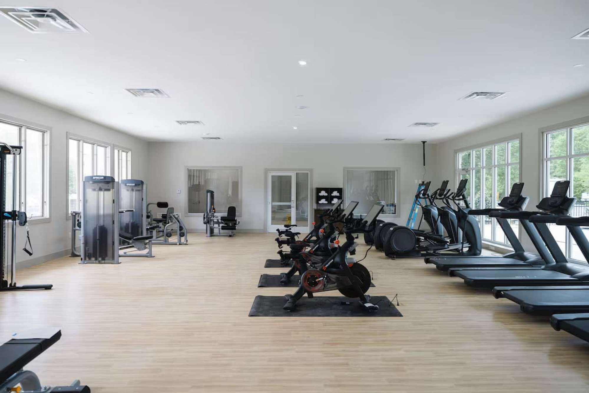 A spacious gym with cardio equipment, weight machines, and a large window providing natural light.