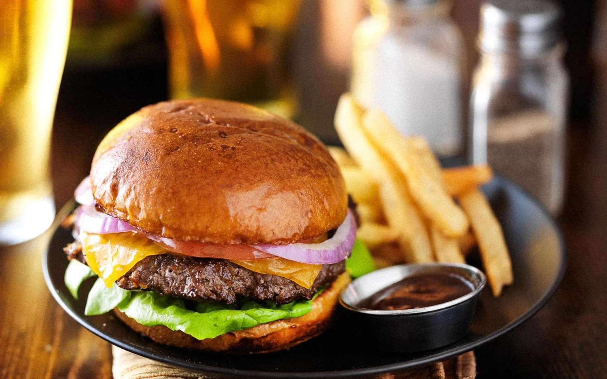 A burger with fries and a small cup of sauce on a plate.