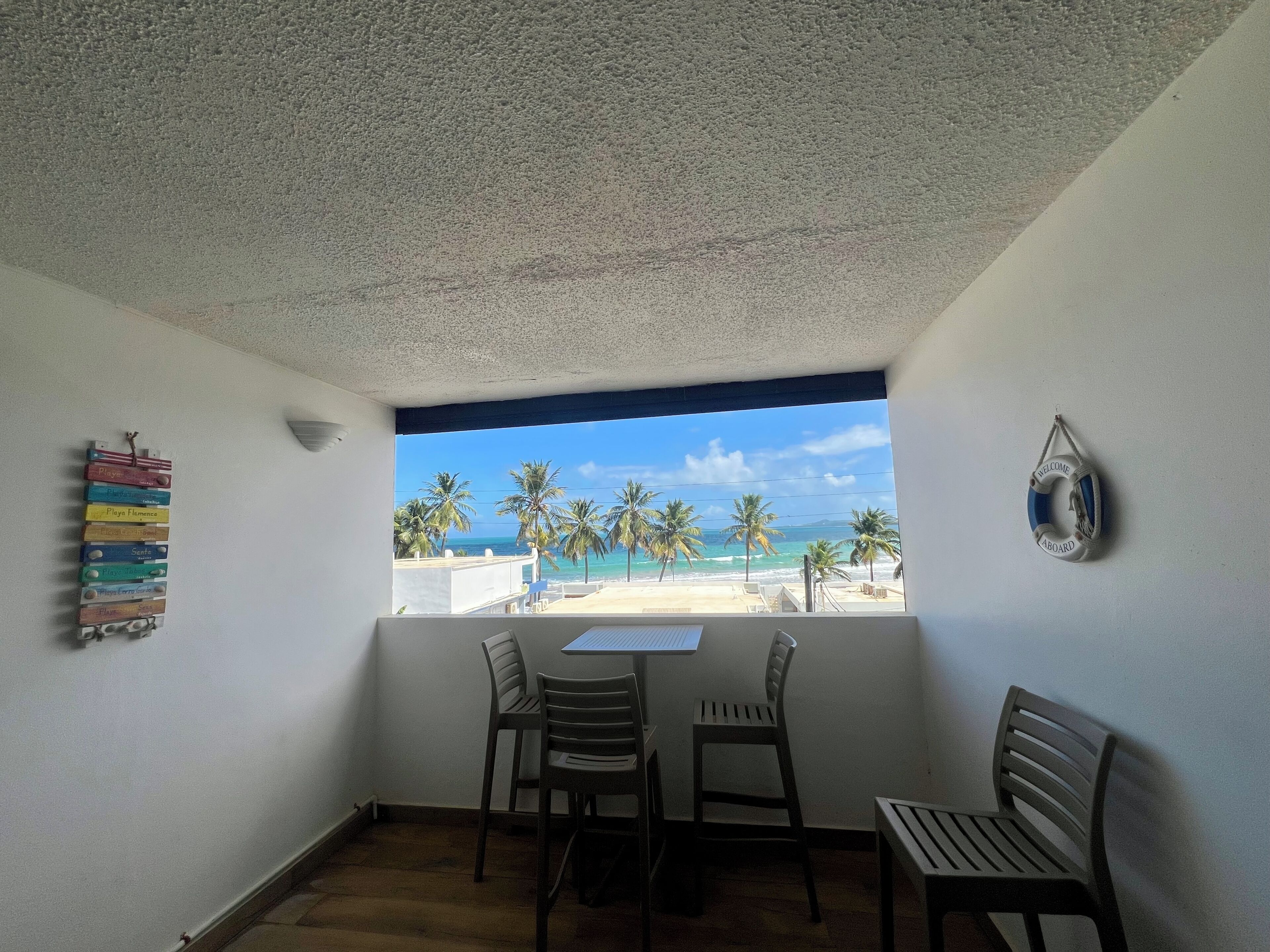 Un balcón con vista a la playa, una mesa con sillas y un cartel en la pared.
