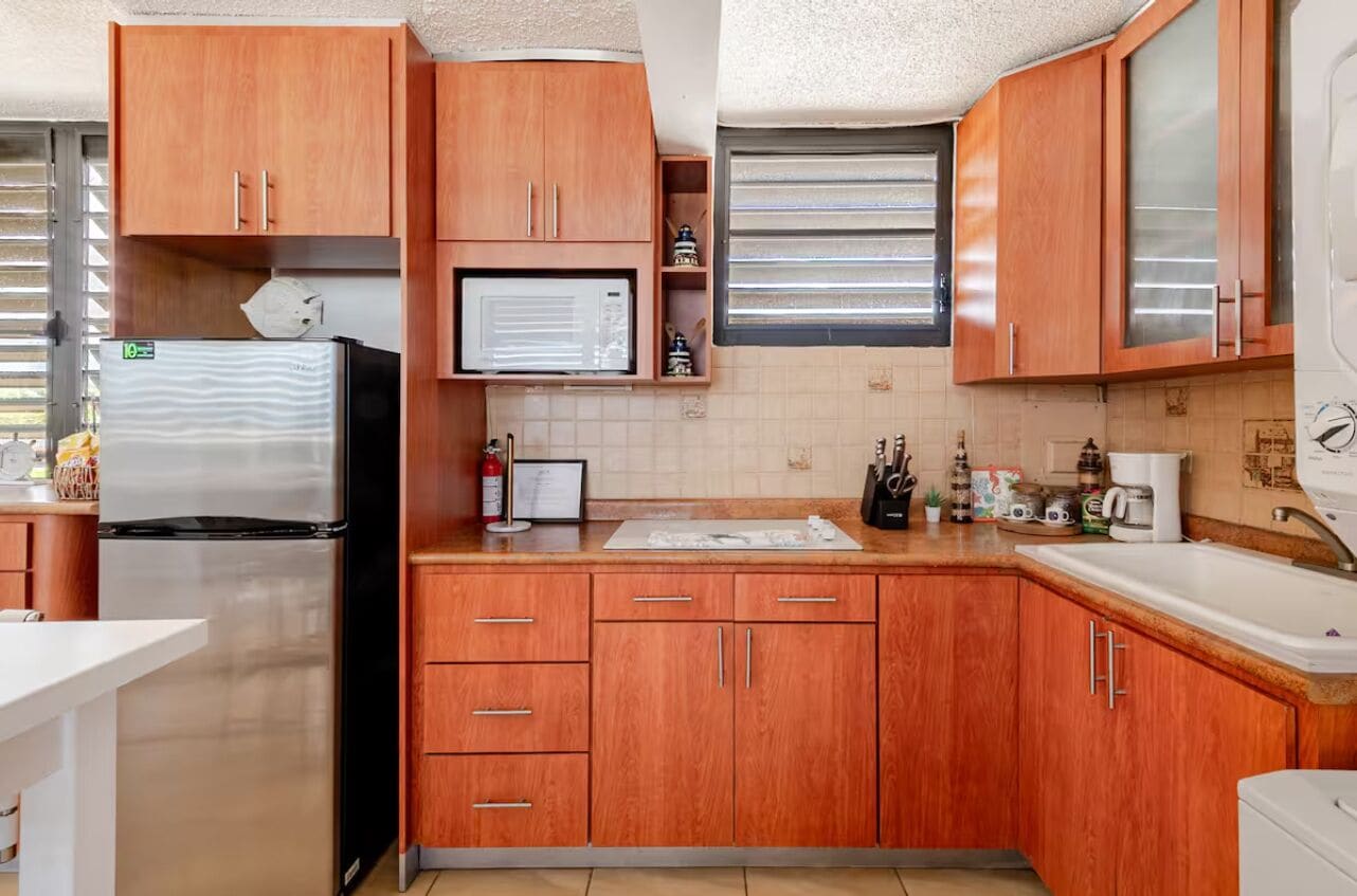Una cocina compacta con armarios de madera, un refrigerador de acero inoxidable, un microondas y un lavamanos.