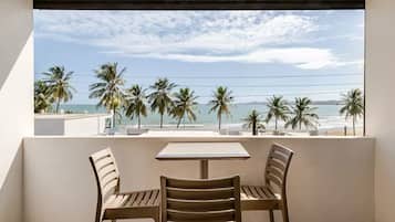Een balkon met een tafel en twee stoelen, uitkijkend op een strand met palmbomen en de oceaan.
