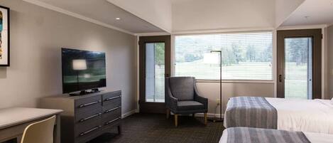 A hotel room with a bed, a desk with a television, a chair, and a window with blinds.