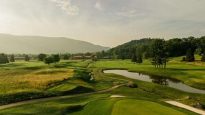 A golf course with a winding water feature, a pond, and a backdrop of trees and hills. - Blue Ridge Mountain Views + Pool. Gym. Restaurant. (Waynesville)