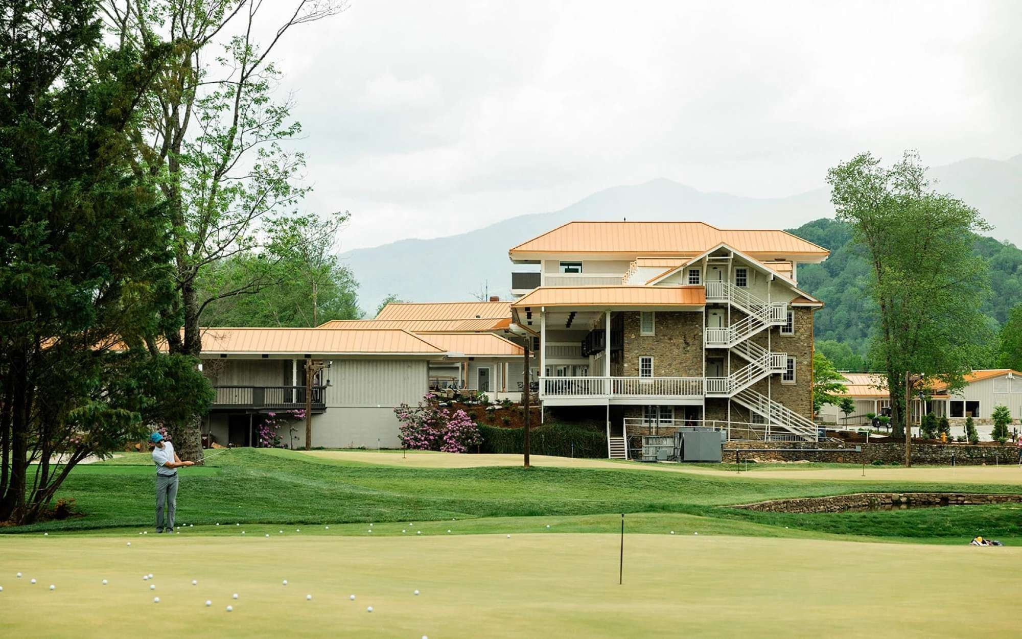 A multi-story building with a stone facade and a balcony, surrounded by a golf course and trees.