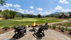 A patio with Adirondack chairs and a fire pit overlooking a golf course with mountains in the background. - Direct Golf Course Access + Pool. Gym. Restaurant. (Waynesville)