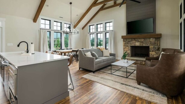 A spacious living area with a stone fireplace, a dining area, and a kitchen with a large island. - Direct Golf Course Access + Pool. Gym. Restaurant. (Waynesville)