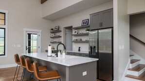 A modern kitchen with a central island, bar stools, a stainless steel refrigerator, and built-in shelves. - Direct Golf Course Access + Pool. Gym. Restaurant. (Waynesville)
