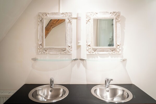 A bathroom with two sinks, a glass shelf, and ornate mirrors.