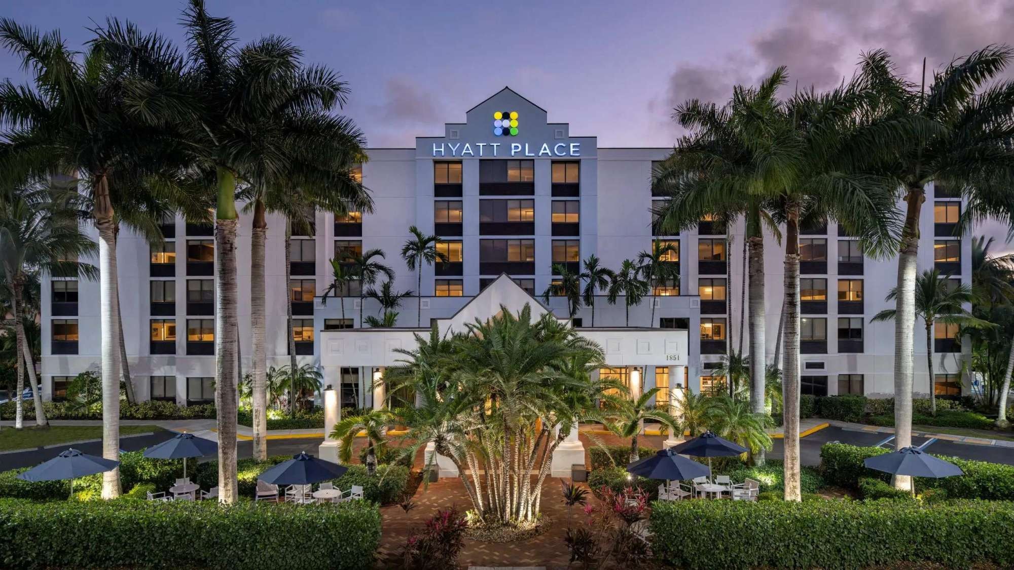 Een Hyatt Place hotel met een symmetrische gevel, palmbomen en terrasjes.