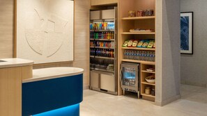 Een hotel receptie met een balie, een drankkoeler vol met dranken en schappen met snacks.