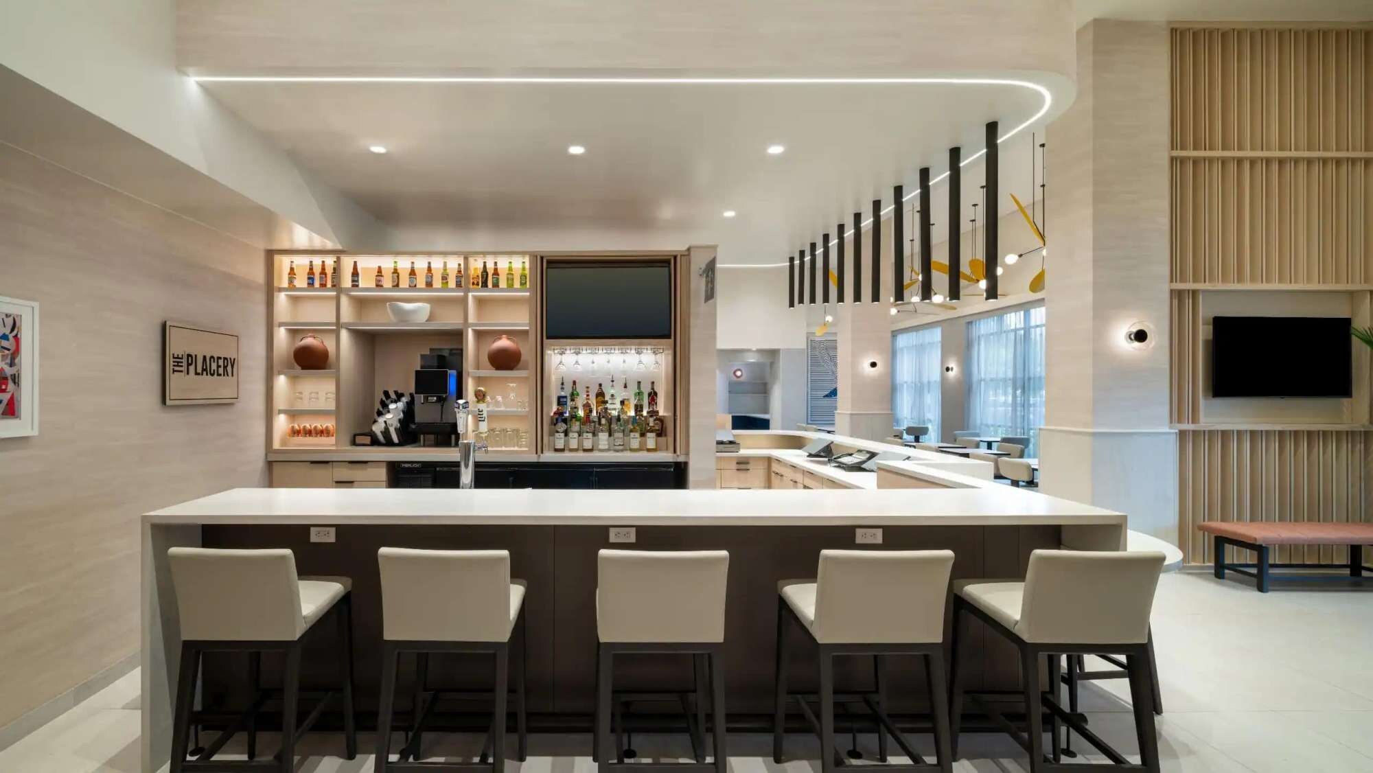 A modern bar area with a central island, bar stools, and a variety of bottles.