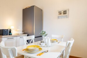 A modern kitchen with white cabinetry, a grey refrigerator, and a dining table set with yellow plates and white bowls. - San Frediano Panoramic Terrace (Firenze)