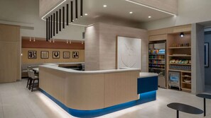 Un espace d  ’accueil moderne doté d’un comptoir incurvé, de sièges, d’un réfrigérateur rempli de boissons et d’un mur orné d’œuvres d’art abstraites.