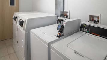A commercial laundry area with two front-loading washing machines, a control panel, and a payment terminal.