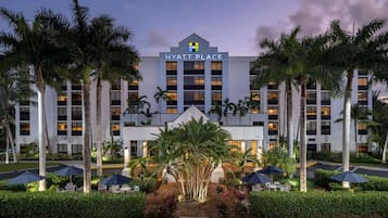 A Hyatt Place hotel with a symmetrical facade, palm trees, and outdoor seating areas.