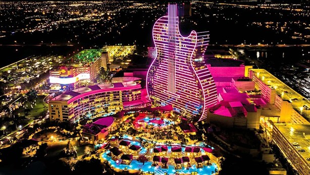 Ein großes Hotel mit einem markanten, gitarrenförmigen Gebäude, mehreren Schwimmbecken und einem gut beleuchteten Außenbereich.