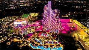 Ein großes Hotel mit einem markanten, gitarrenförmigen Gebäude, mehreren Schwimmbecken und einem gut beleuchteten Außenbereich.