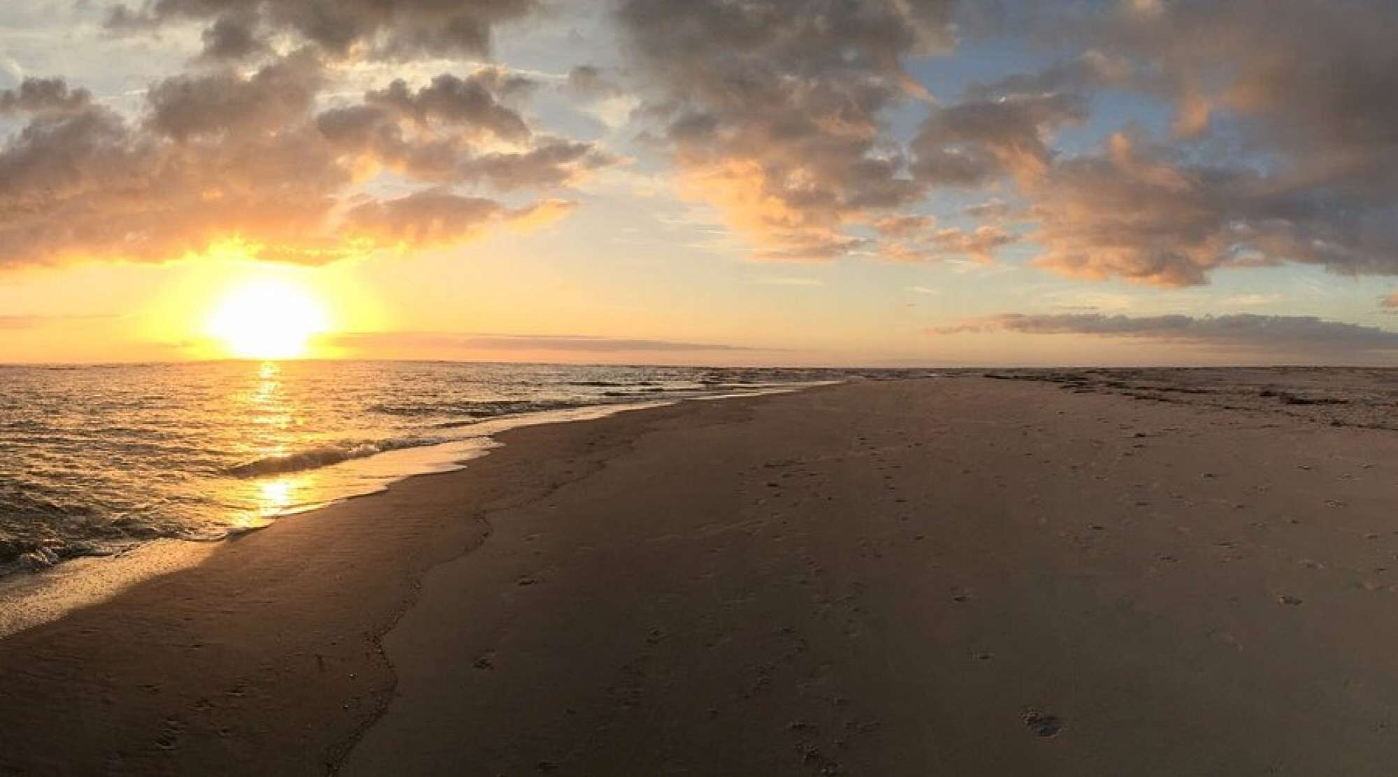 Una spiaggia con impronte che conducono verso l'oceano, sotto un cielo al tramonto.
