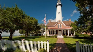 A lighthouse with a brick base and white walls, surrounded by a white picket fence and lush greenery. - Direct Marshlands Views + Golf. Pool. Restaurant. (St. Simons Island)