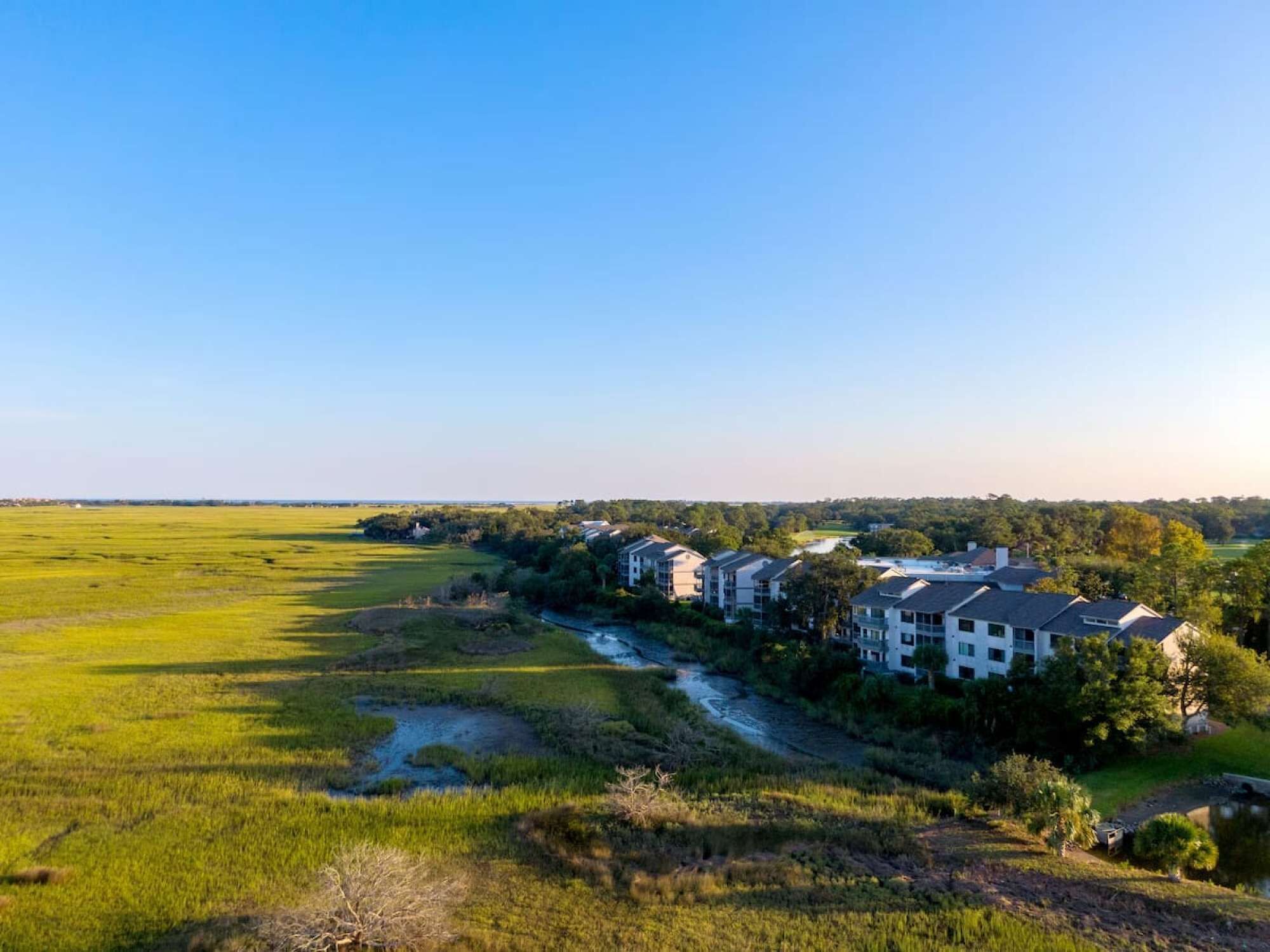 Una zona residencial con varias casas de dos pisos, un río y un amplio campo verde.