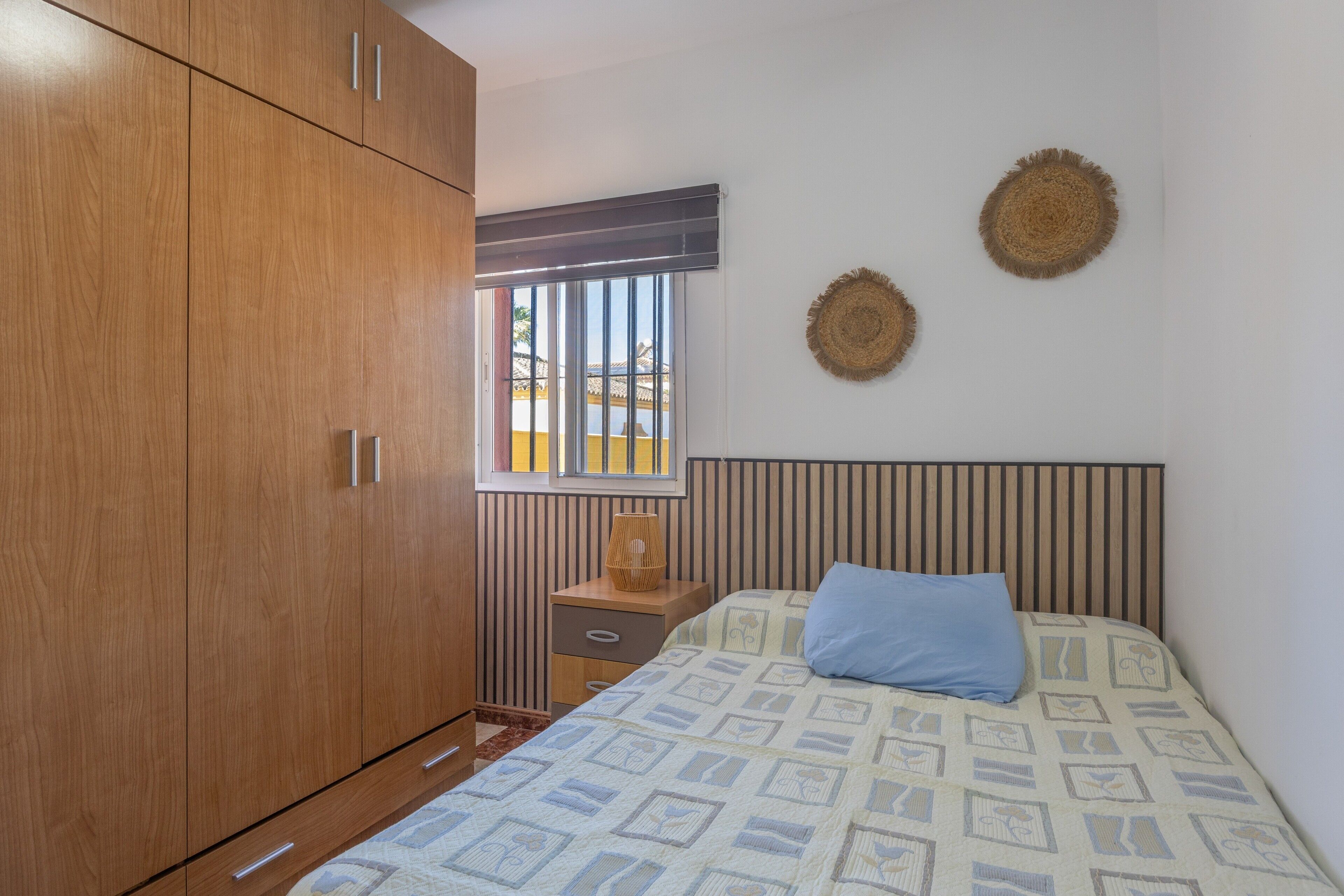 A bedroom with a bed, a wardrobe, a bedside table, and a window.