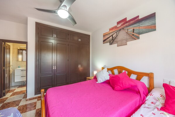 A bedroom with a bed, a wardrobe, a ceiling fan, and a wall art piece.