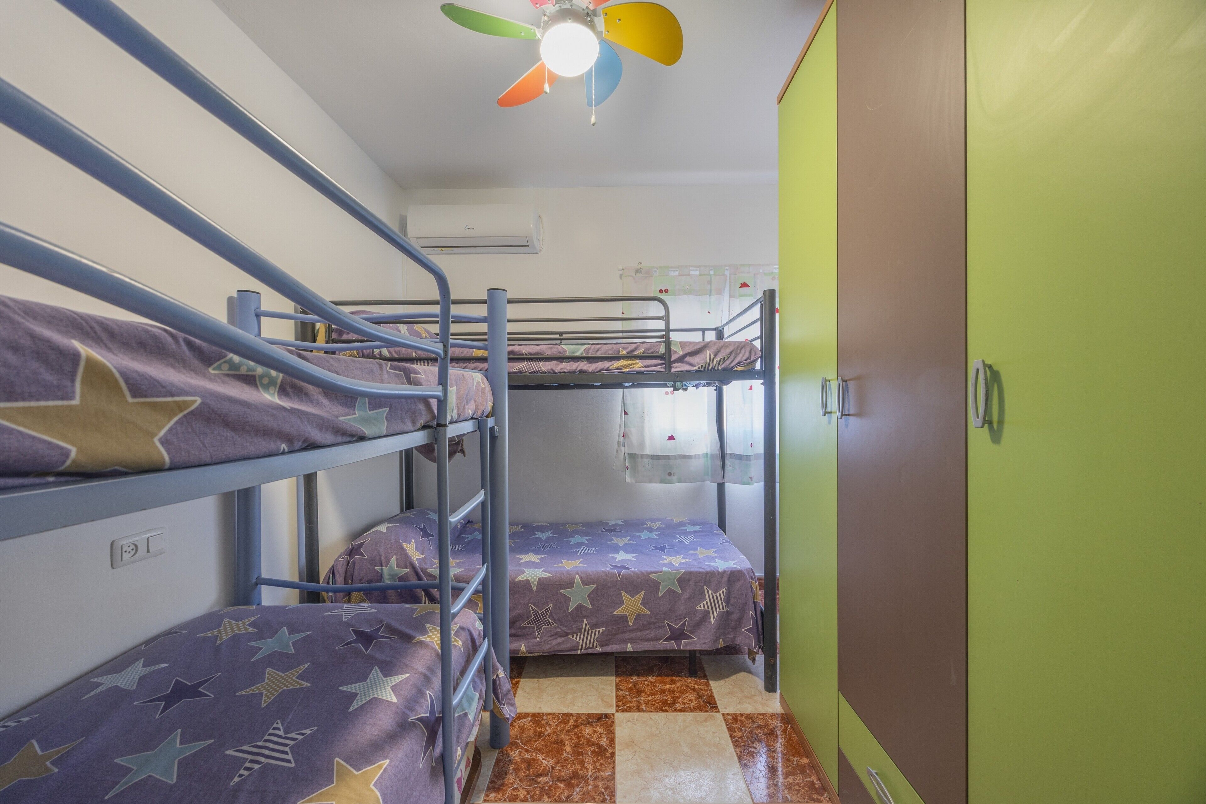 A bunk bed room with a ceiling fan, a window with curtains, and a green door.