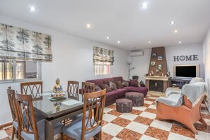 A living room with a sofa, a TV, a fireplace, and a dining area with chairs and a table.