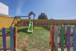 A playground with a slide and climbing structures, surrounded by a fence.