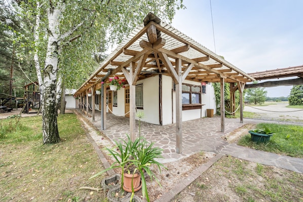 Un espacio al aire libre techado con una pérgola de madera, una planta en maceta y un sendero de piedra que lleva a un edificio.