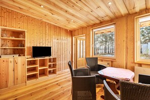 Un interior de madera con televisor, estanterías, sillas de mimbre y una mesa.