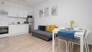 A modern kitchen with white cabinets, a grey sofa, and a dining table with a blue tablecloth. - Bright Apartment with Bathtub | Balcony and Good Communication (Warszawa)