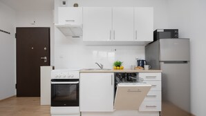 A compact kitchen with white cabinets, a built-in oven, a dishwasher, and a refrigerator. - Bright Apartment with Bathtub | Balcony and Good Communication (Warszawa)