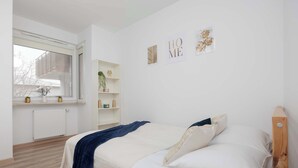 A bedroom with a bed, a window, a radiator, and wall decorations. - Bright Apartment with Bathtub | Balcony and Good Communication (Warszawa)