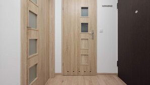 A hallway with a wooden door featuring multiple glass panels and a modern handle. - Bright Apartment with Bathtub | Balcony and Good Communication (Warszawa)
