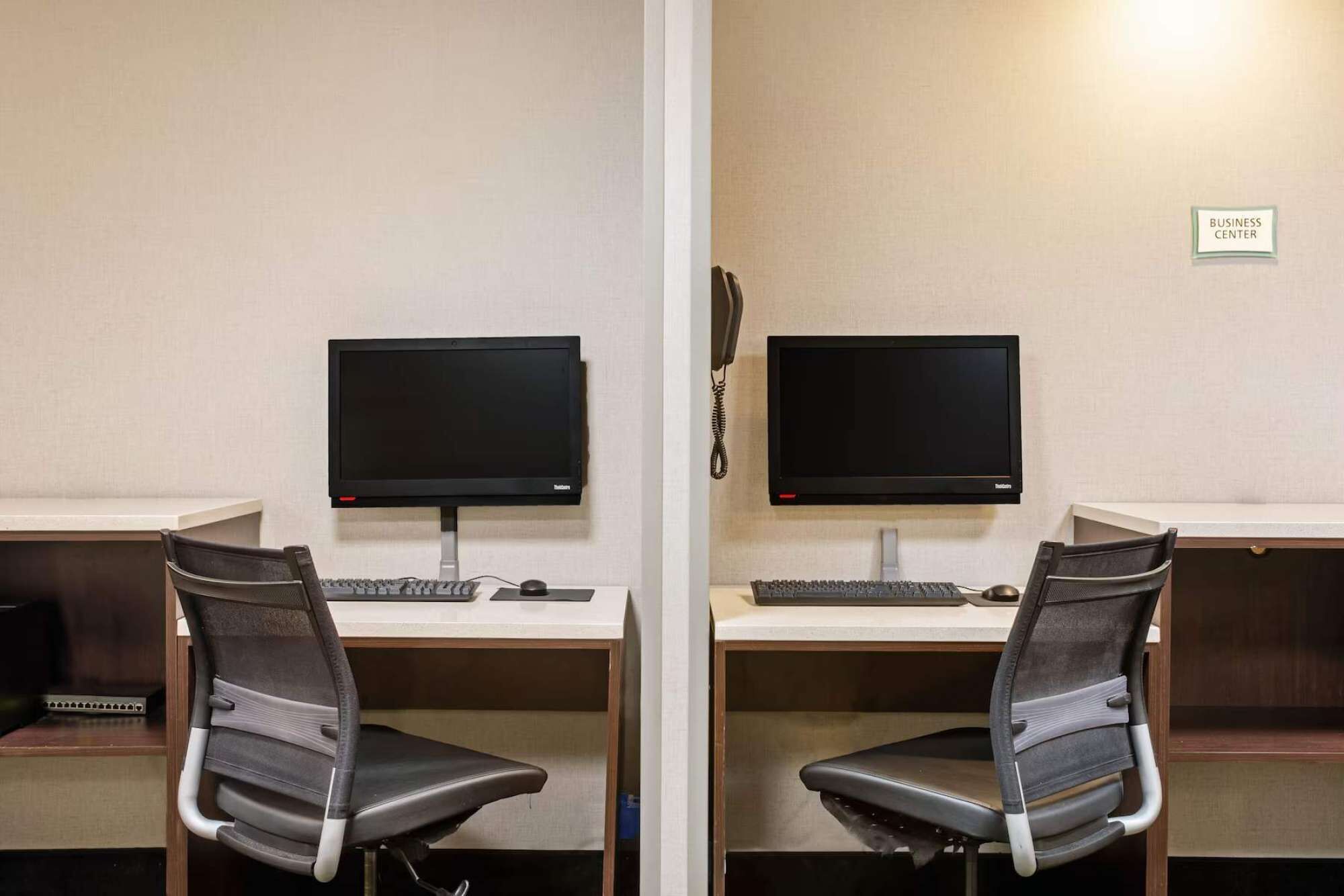A mirrored office setup with two desks, each with a computer monitor, keyboard, and ergonomic chair.