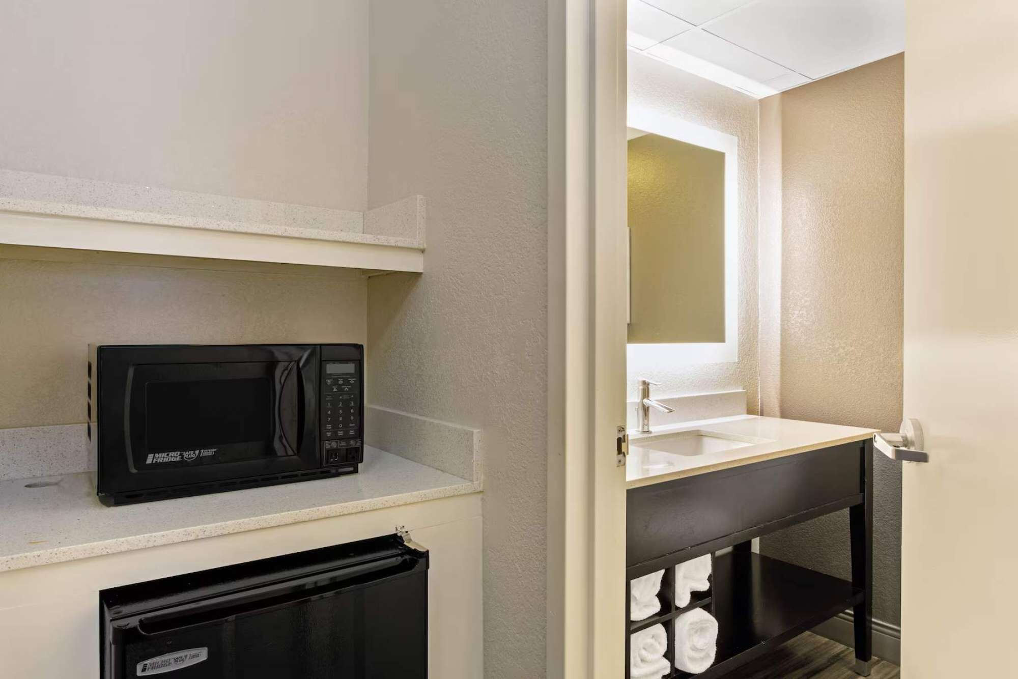 A compact bathroom with a microwave on a shelf, a sink with a mirror above it, and a towel rack with folded towels.