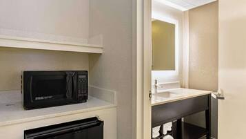 A compact bathroom with a microwave on a shelf, a sink with a mirror above it, and a towel rack with folded towels.
