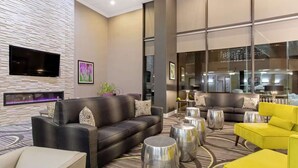 Un hall d’hôtel moderne avec un canapé en cuir noir, un fauteuil jaune et une cheminée.